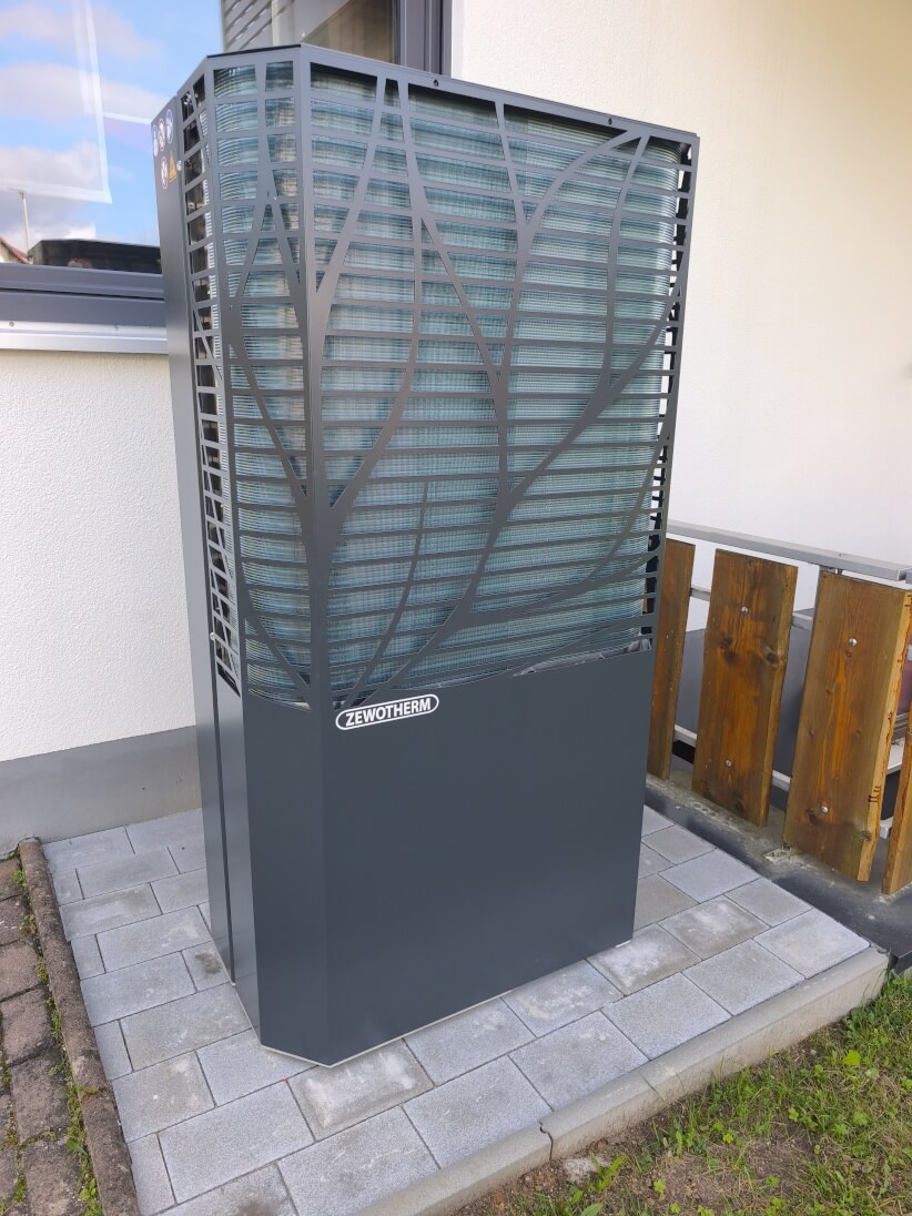 Moderne LAMPDA Wärmepumpe mit elegantem Design im Freien Eine moderne LAMPDA Wärmepumpe mit einem eleganten Design, die an einer Hauswand auf einem gepflasterten Bereich steht.